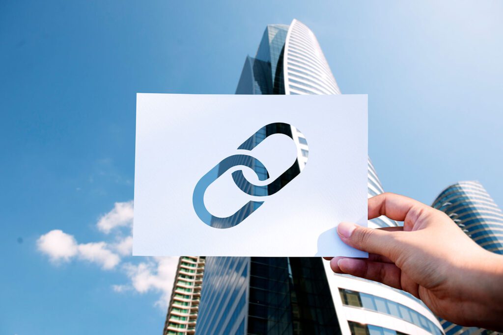 Hand holding a paper with a chain link icon against skyscrapers and blue sky.