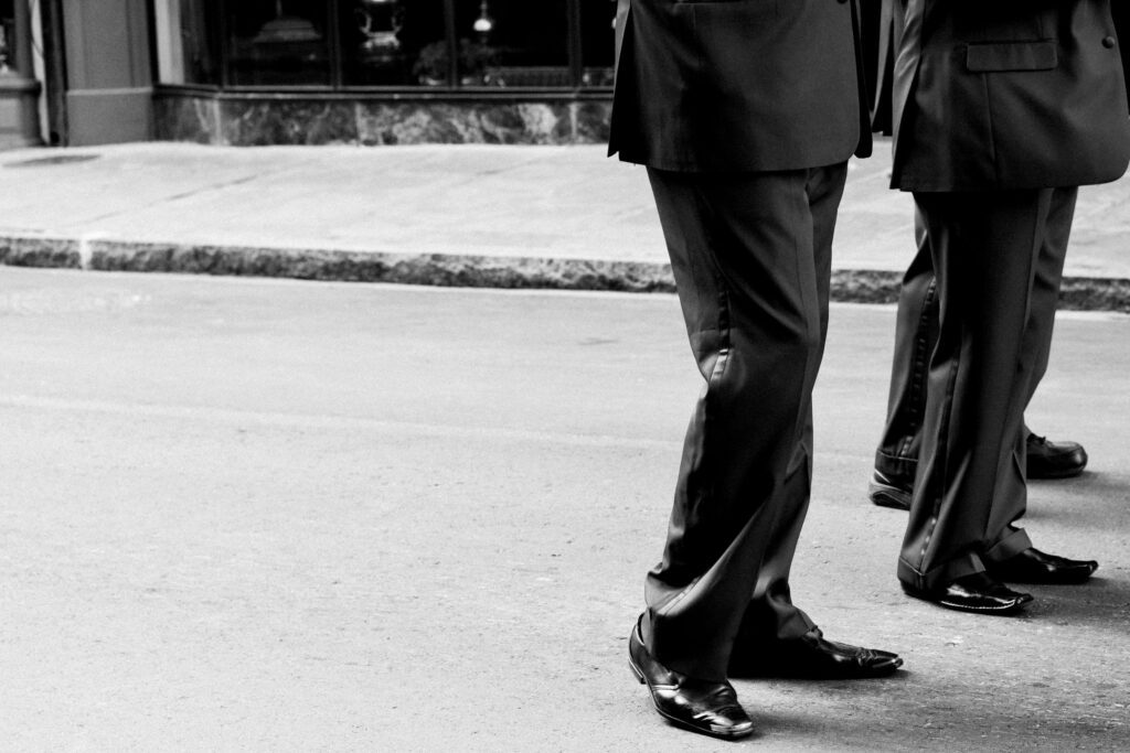 Two people walking on a paved street wearing formal suits and dress shoes.