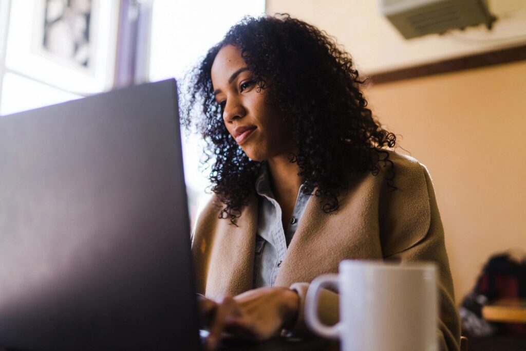 Woman working thoughtfully on her laptop with a coffee cup nearby.