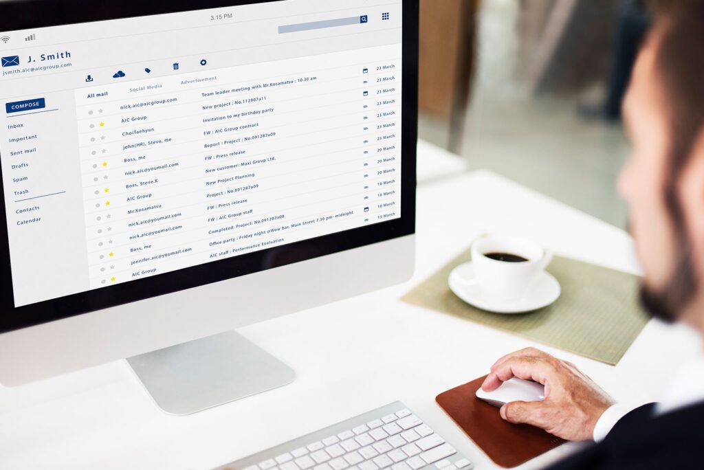 Person managing emails on a desktop computer with coffee nearby.