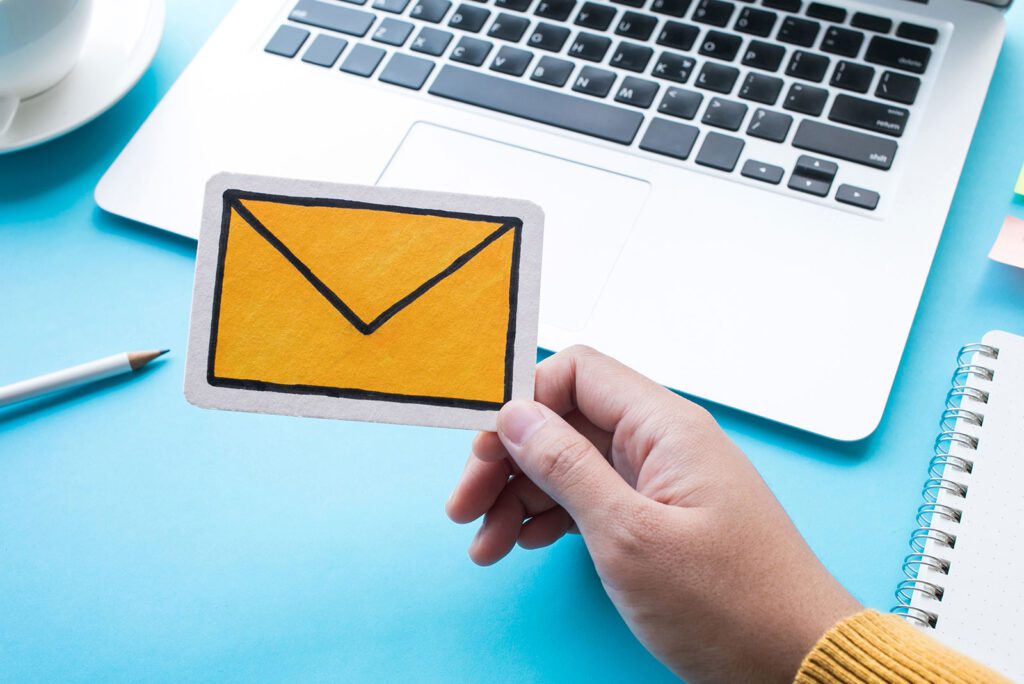 Hand holding a paper envelope icon in front of a laptop keyboard.