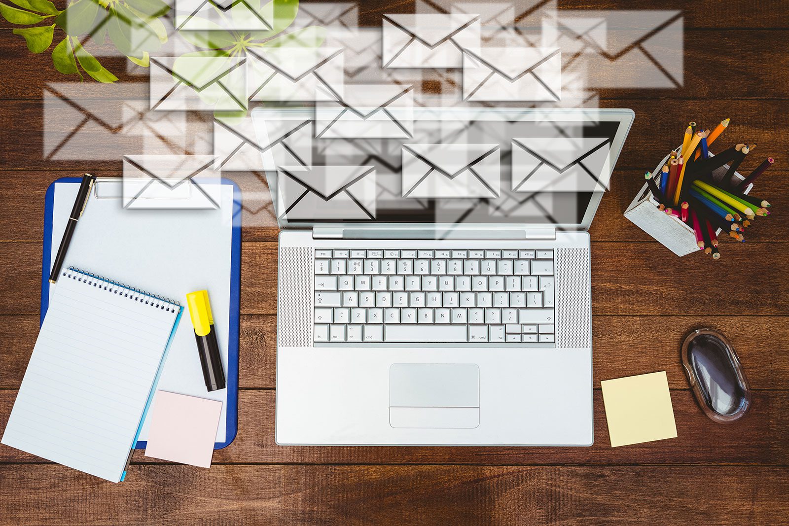 A laptop surrounded by floating email icons on a wooden desk.