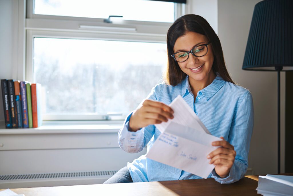 Woman happily reading mail at home near a window.