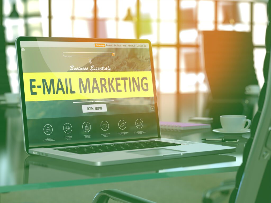 Laptop displaying E-mail Marketing on screen in a bright office.