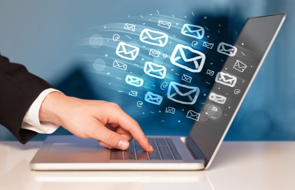 Hand typing on laptop with digital email icons floating above.