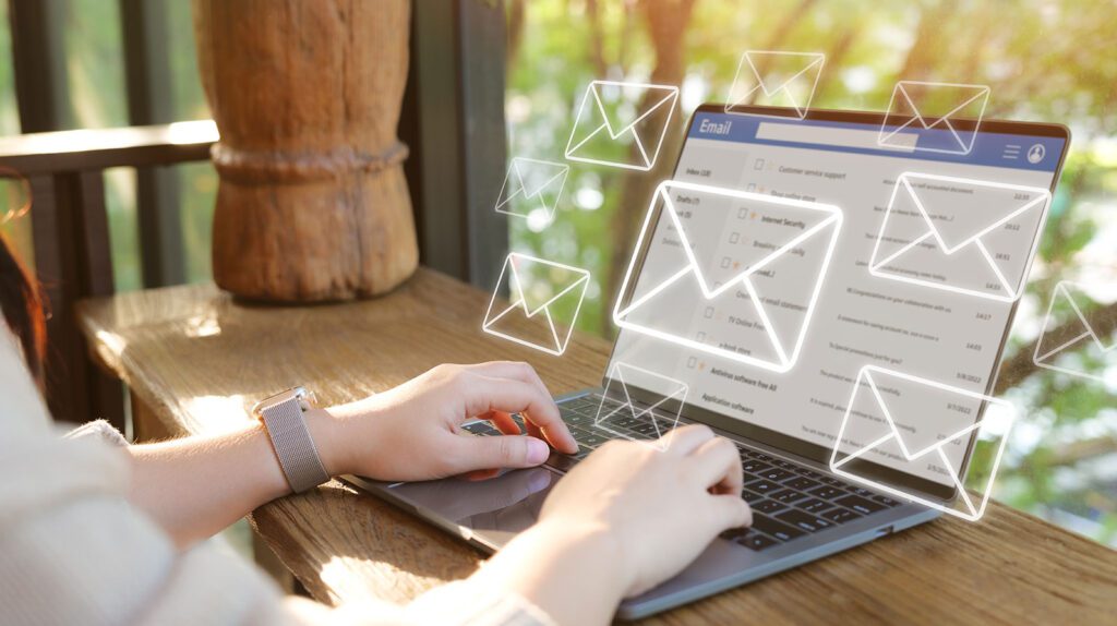 Person typing on laptop with digital email icons floating above.