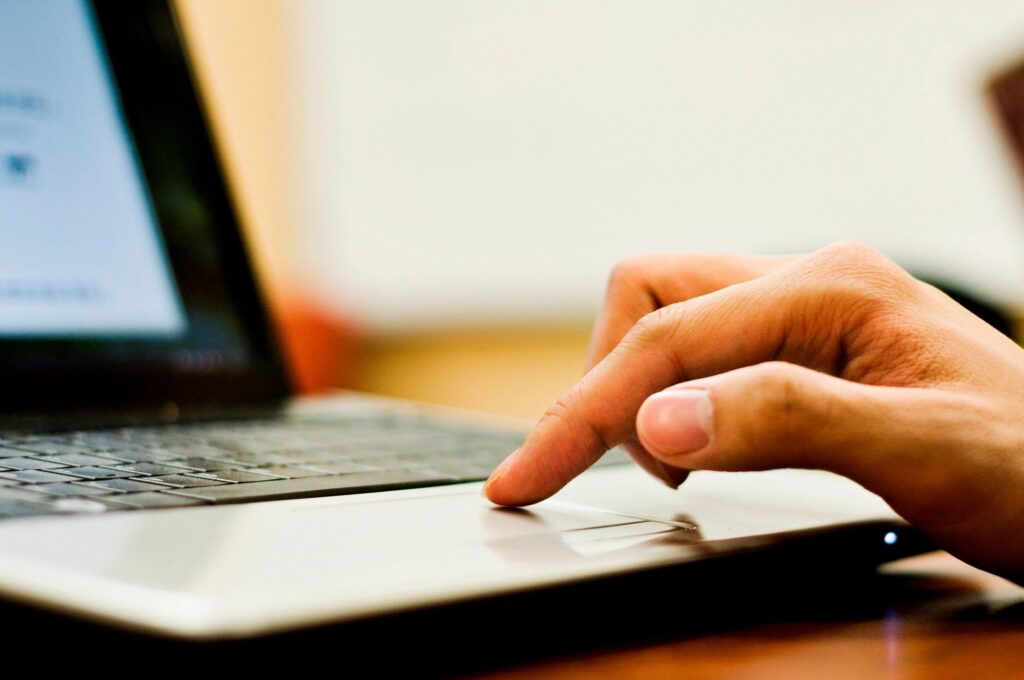 Finger touching a laptop trackpad, focusing on hand and device.