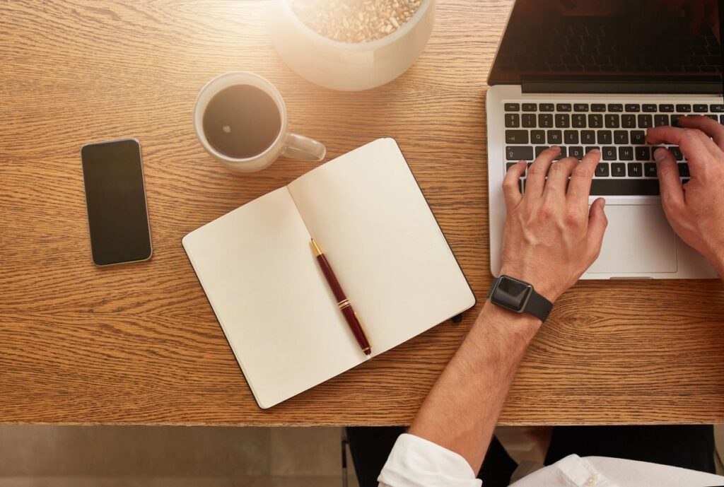 Workspace with laptop, notebook, coffee, and hand typing.