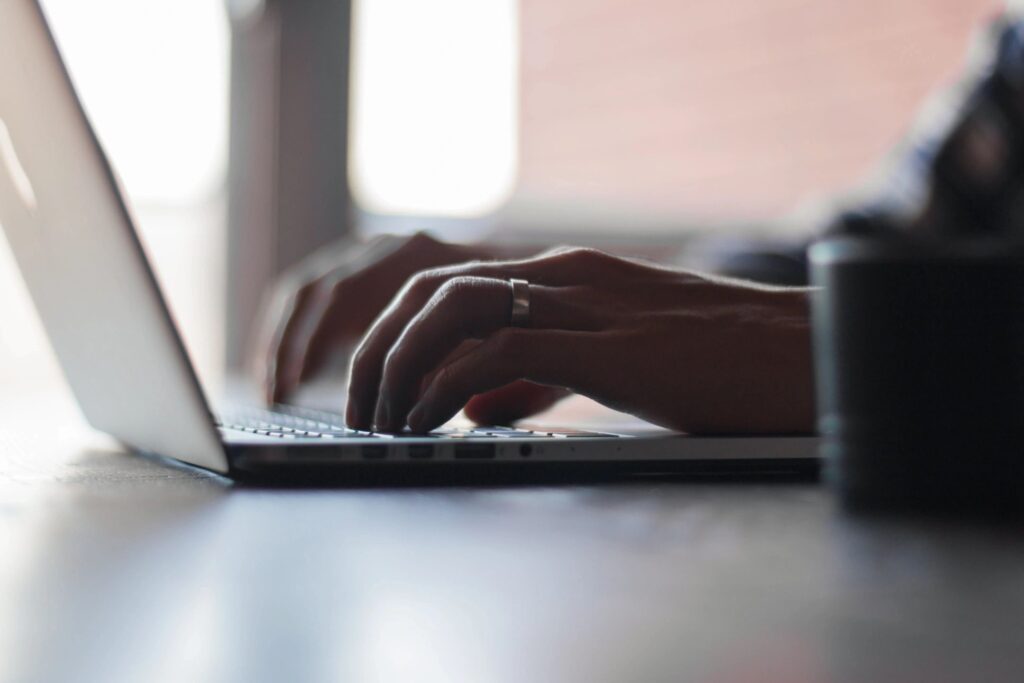 Close-up of hands typing on a laptop keyboard in soft natural light.