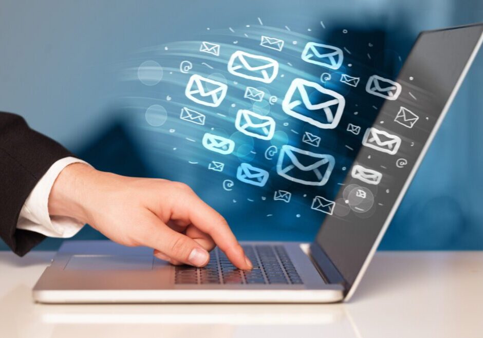 Hand typing on laptop with digital email icons floating above.