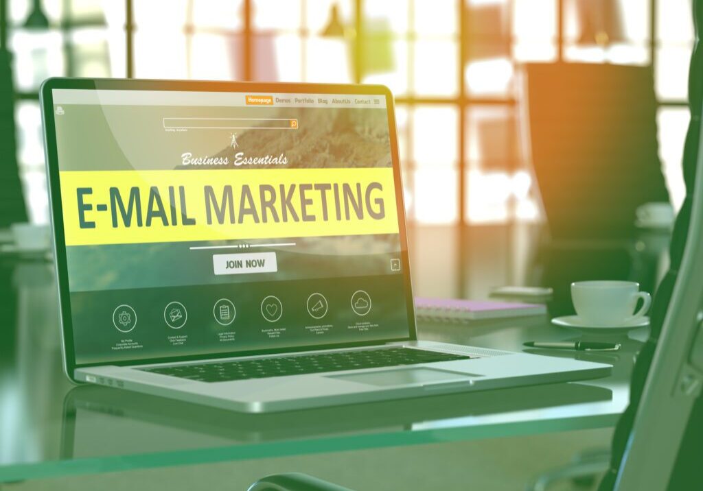 Laptop displaying E-mail Marketing on screen in a bright office.