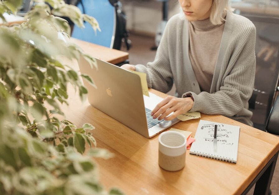Person working on a laptop with a notebook and coffee nearby.