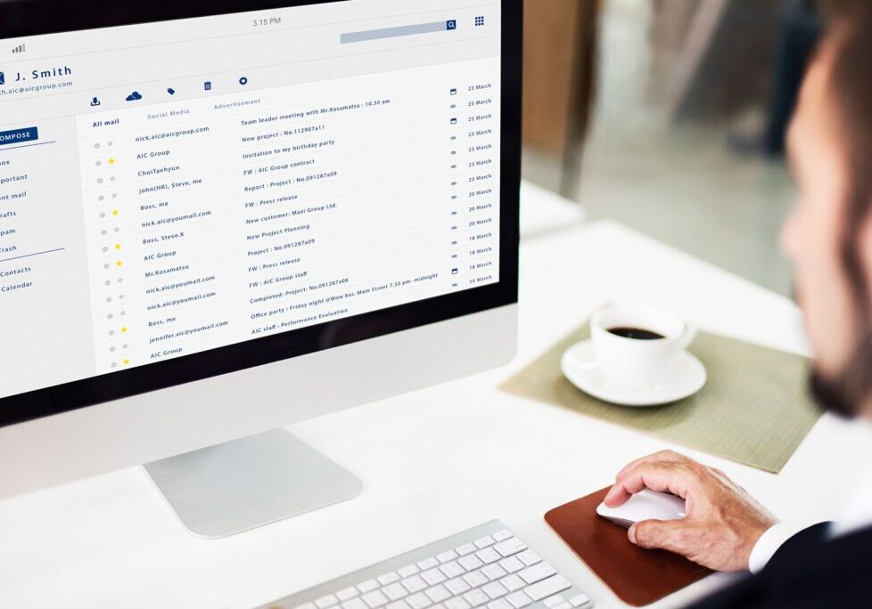 Person managing emails on a desktop computer with coffee nearby.