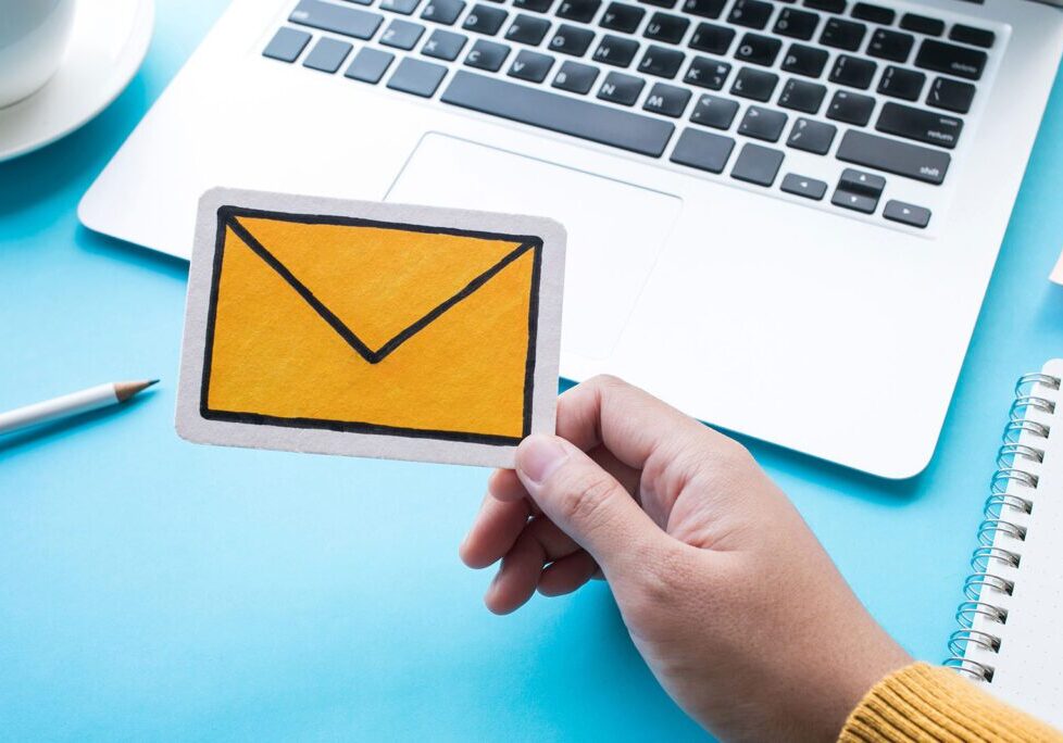 Hand holding a paper envelope icon in front of a laptop keyboard.