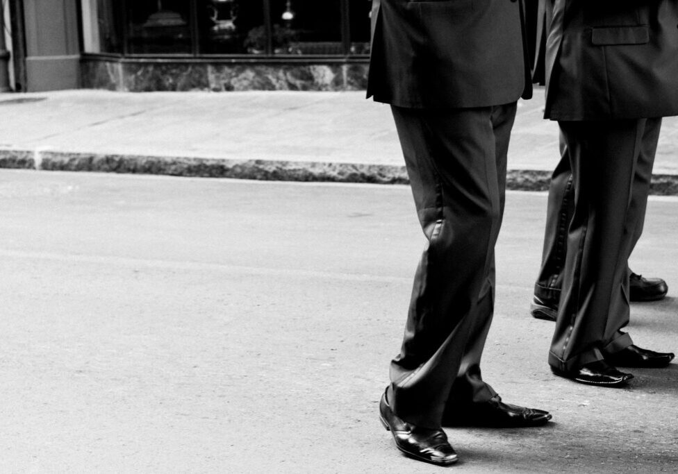 Two people walking on a paved street wearing formal suits and dress shoes.
