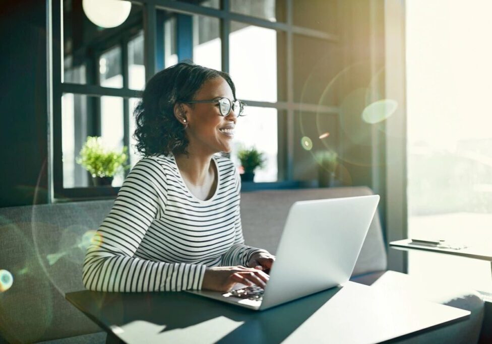 A woman working on a laptop near a window with natural light.
