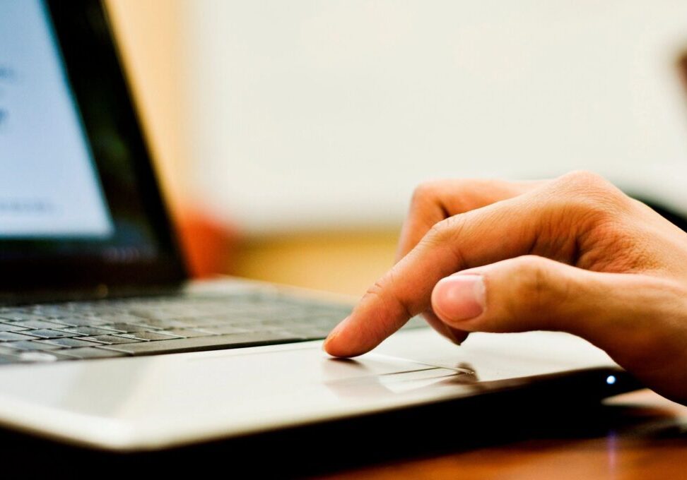 Finger touching a laptop trackpad, focusing on hand and device.