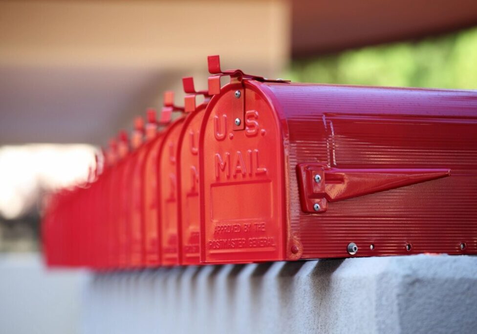 Row of red USPS mailboxes outdoors on a sunny day.