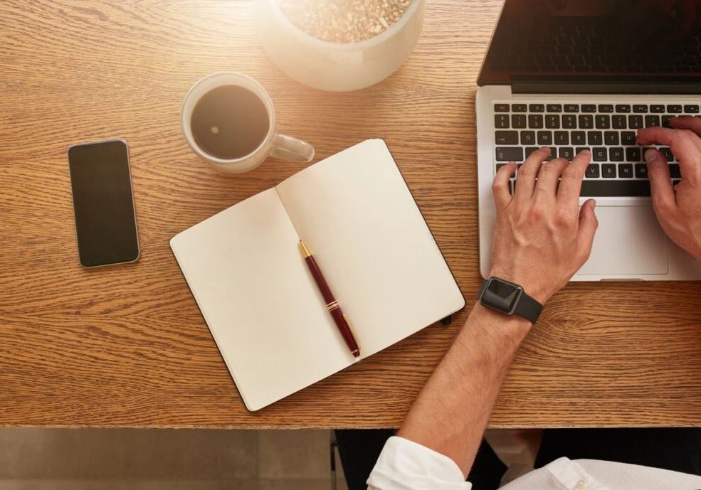 Workspace with laptop, notebook, coffee, and hand typing.