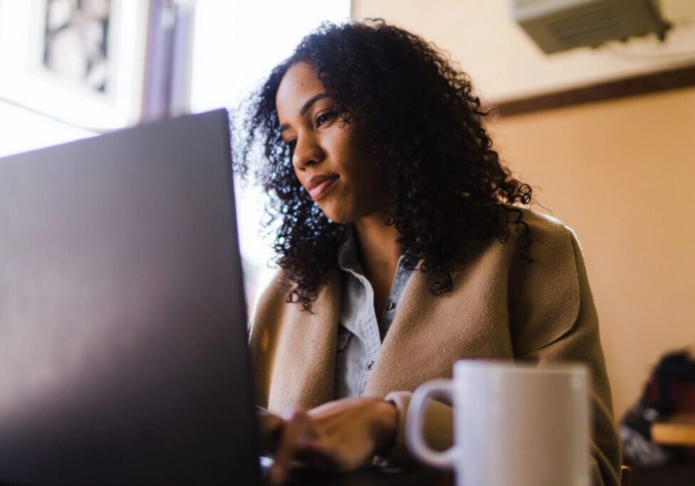 Woman working thoughtfully on her laptop with a coffee cup nearby.