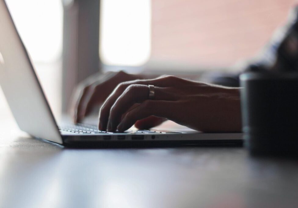 Close-up of hands typing on a laptop keyboard in soft natural light.
