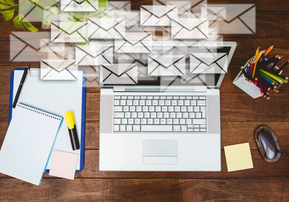 A laptop surrounded by floating email icons on a wooden desk.